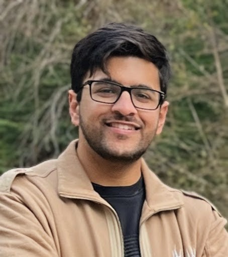 Lokesh Sandhu smiling, wearing glasses and a tan jacket.
